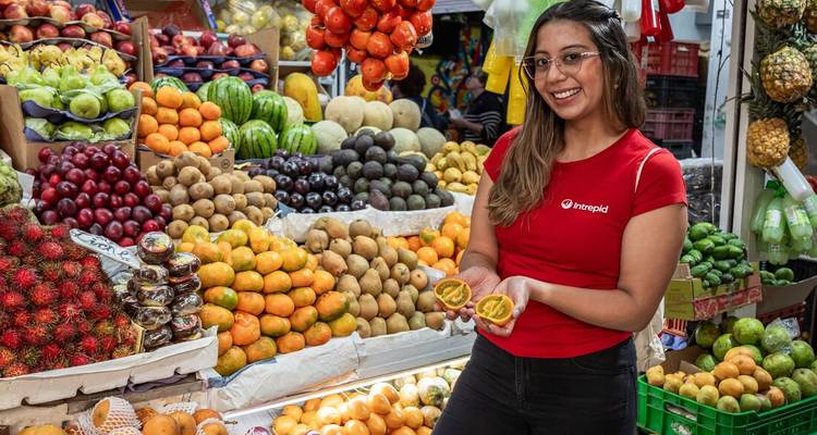 Lächelnder Marktführer hält geschnittene Passionsfrucht zwischen farbenfrohen Stapeln tropischer Früchte
