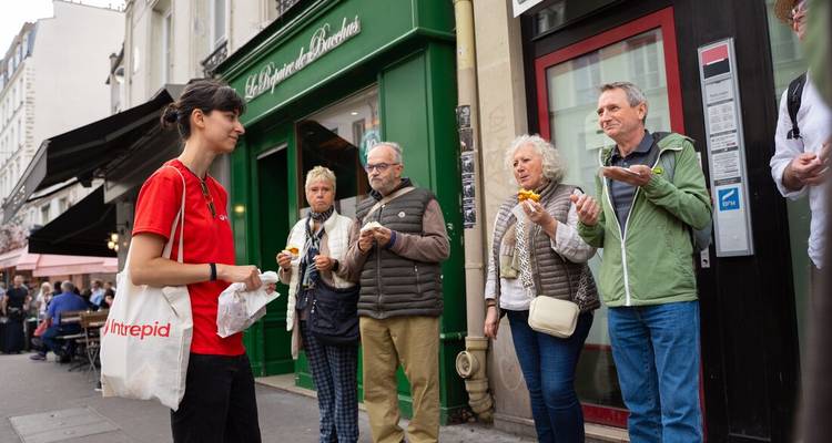 Petit groupe de touristes savourant des pâtisseries devant une boulangerie parisienne sur une rue animée de la ville.