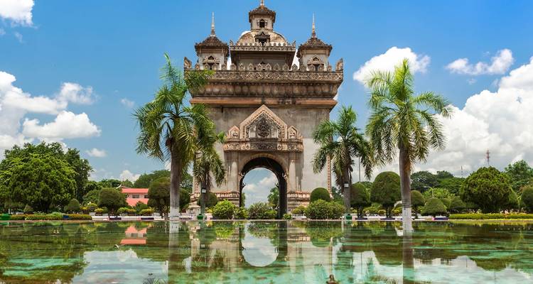 Monumento Patuxai con un reflejo en un estanque bajo un cielo brillante.