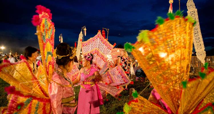 Bailarines tailandeses tradicionales en trajes vibrantes actuando con sombrillas iluminadas en festival nocturno