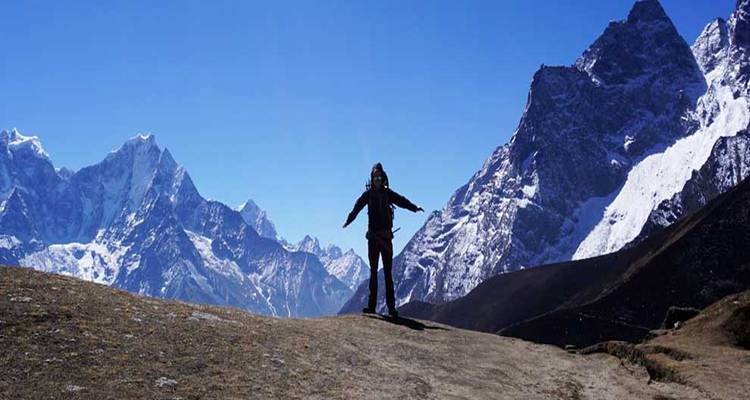 Persona de pie con los brazos extendidos contra un telón de fondo de montañas cubiertas de nieve.