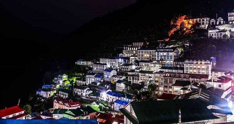 Vista nocturna de un pueblo montañoso iluminado con luces.