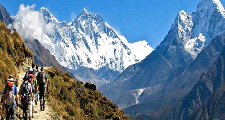 Grupo de excursionistas en un sendero con montañas cubiertas de nieve al fondo.