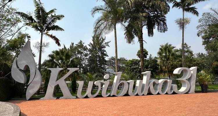 Panneau Kwibuka31 entouré de palmiers et de ciel dégagé.