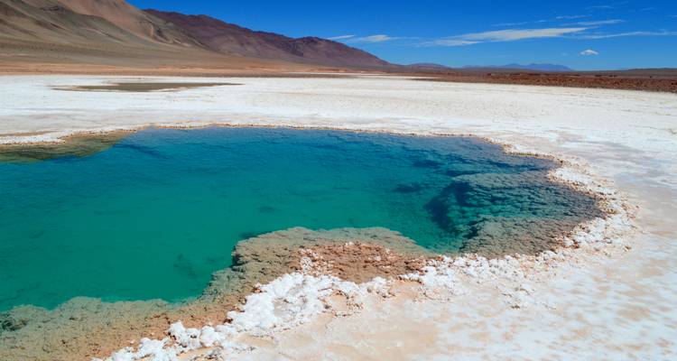 Strahlend blaues Wasser in einer mineralreichen Landschaft mit fernen Bergen.