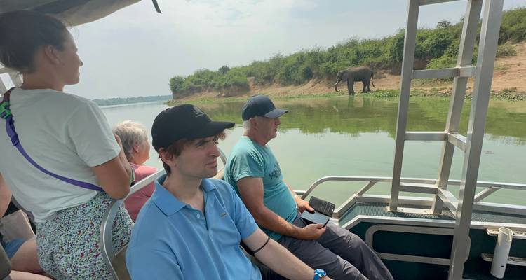 Des gens lors d'un safari en bateau observant des éléphants sur la berge.