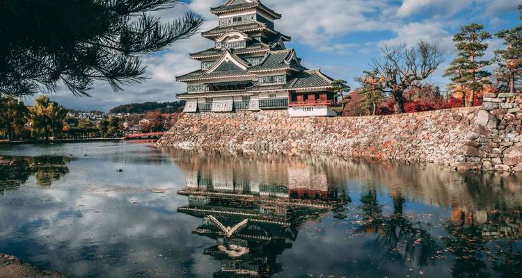 Château japonais avec reflet de douves sous un ciel dégagé.