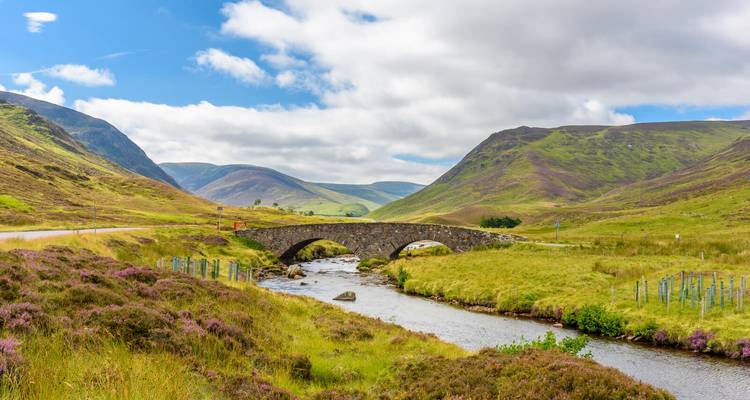 Steinbrücke über einen Fluss in einem grünen Tal.