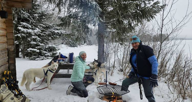 People and sled dogs around a picnic table in a snowy setting.