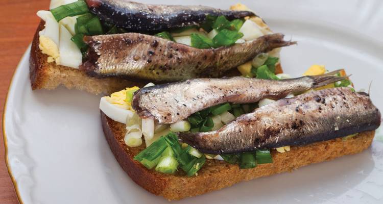 Open-faced sandwich with fish, egg, and green onions on rye bread.