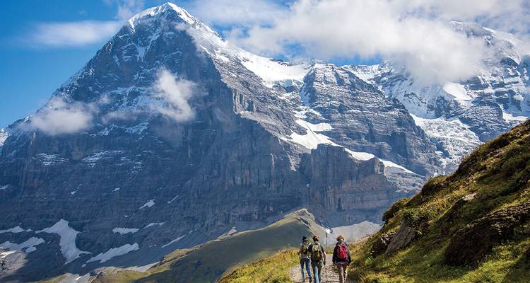Hikers on a trail with mountains and clouds in the backdrop.