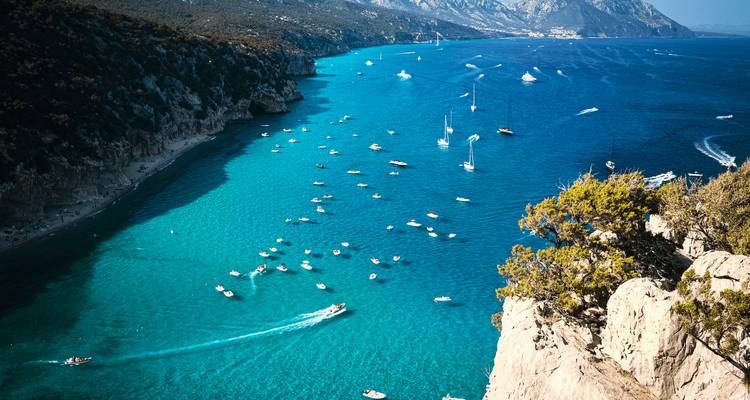 Une vue aérienne d'une baie turquoise remplie de petits bateaux, entourée de falaises.
