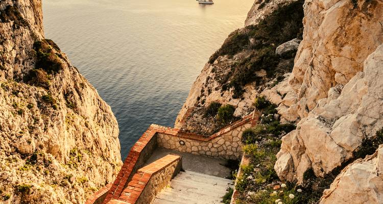 Un sentier de pierre escarpé menant vers une mer calme, flanqué de falaises rocheuses.