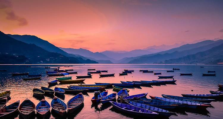 Pequeños barcos en un lago rodeado de montañas al atardecer.