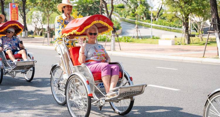 Los visitantes disfrutan de un paseo en ciclo por una calle soleada de la ciudad, saludando y sonriendo a la cámara