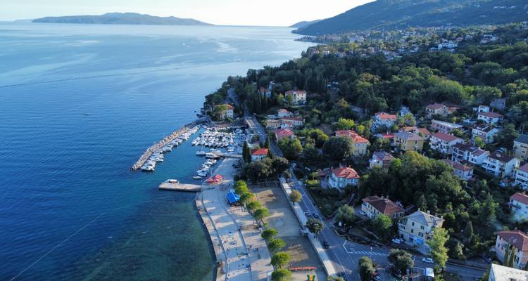 Luftaufnahme einer Küstenstadt mit einem Jachthafen und Hügeln im Hintergrund.