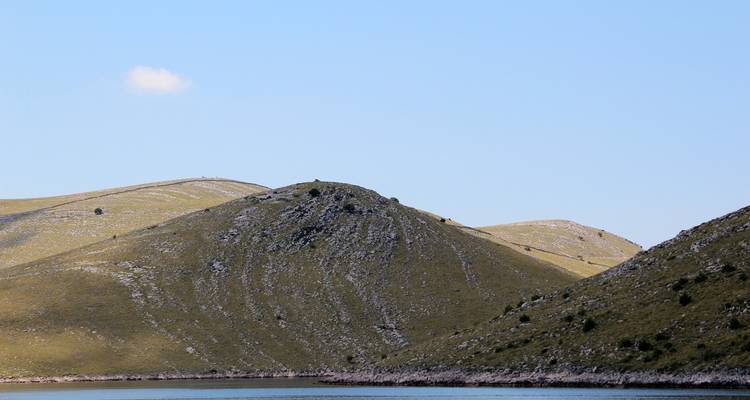 Sanfte Hügel mit spärlicher Vegetation und einem ruhigen blauen Meer.