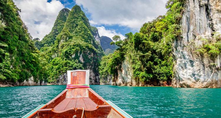 Front view from a boat sailing towards lush limestone formations.