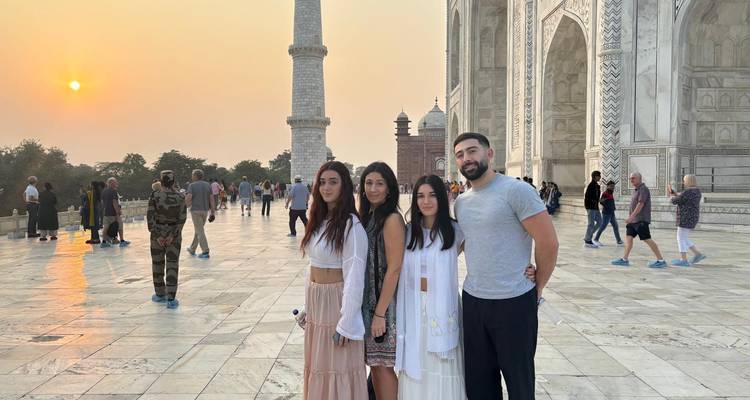 Groupe de personnes posant devant le Taj Mahal avec un coucher de soleil en arrière-plan.