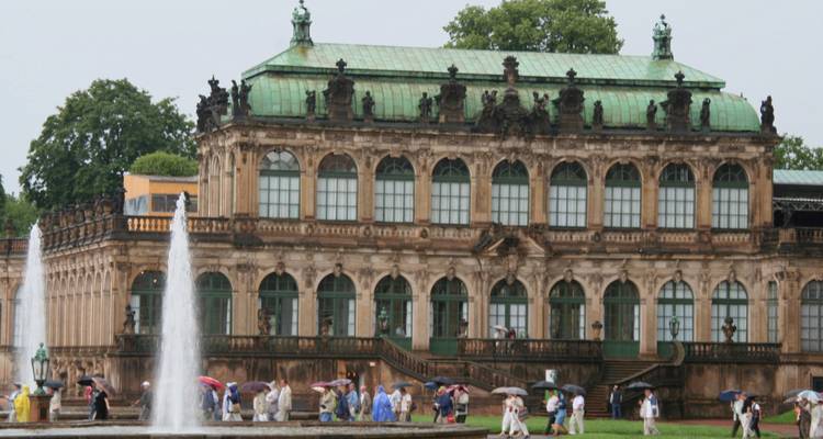 Palais de Zwinger à Dresde avec des touristes marchant sous la pluie.