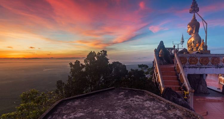 Statue de Bouddha dorée au coucher de soleil avec ciel coloré.