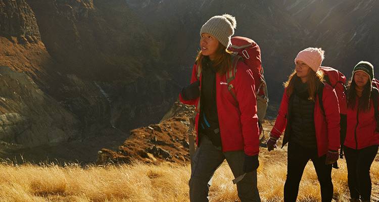 Hikers in warm gear walking through a grassy mountain area in Nepal.