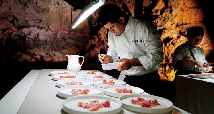Chef preparing dishes in a cave kitchen setting.
