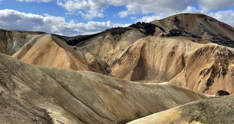 Paysage montagneux aride avec des crêtes colorées et un ciel bleu.