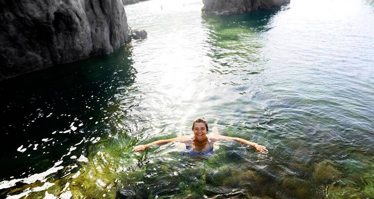 Smiling person swimming in clear water between rocky formations.