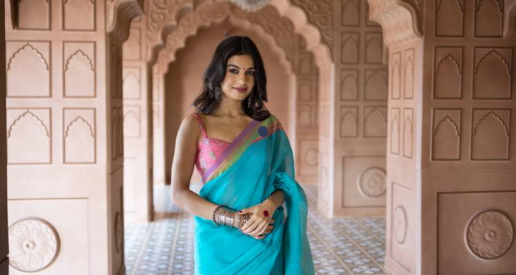 Frau in traditionellem Sari steht in einem kunstvoll gestalteten Korridor.