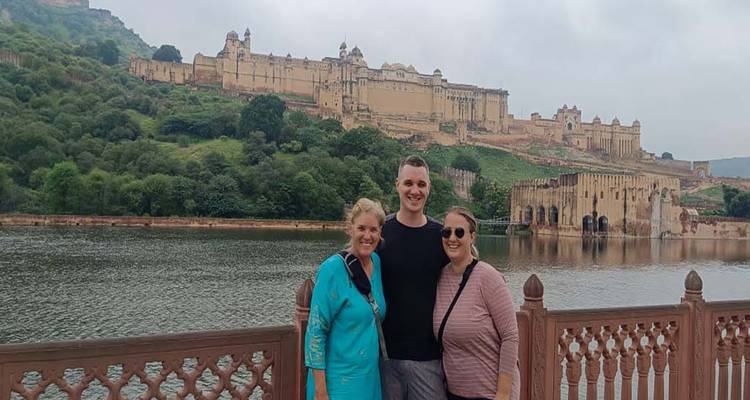 Three people posing beside a lake with a large fort in the background.