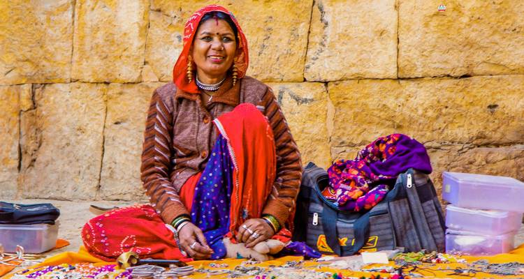 Einheimische Frau sitzt vor einer Wand und verkauft bunten Schmuck.