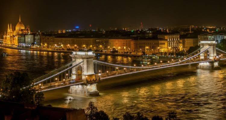 Vista nocturna de un puente iluminado sobre un río junto al paisaje urbano.