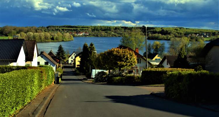 A suburban street leading to a scenic lake under a dramatic sky.