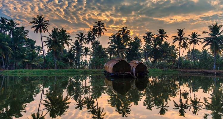 Sunset over backwaters with houseboats and palm trees reflected in the water.
