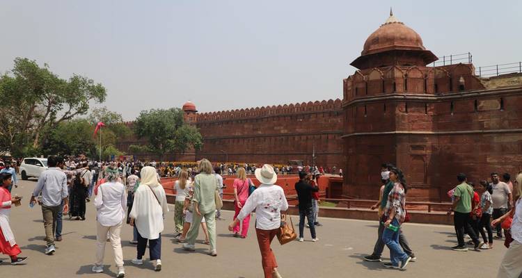 Large group of tourists in front of a historic red stone fort wall.