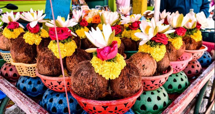 Decorative coconut offerings with flowers in colorful bowls displayed on a market stand.