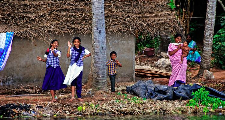 Children smiling and playing near a thatched house by the riverbank.
