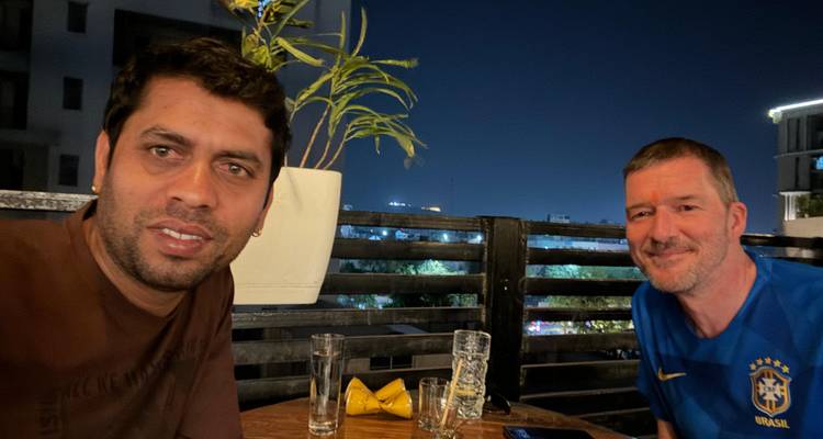 Deux hommes assis à une table sur un balcon la nuit.