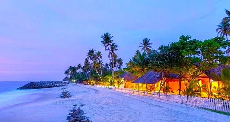 Strand met palmbomen en kleurrijke gebouwen bij zonsondergang.
