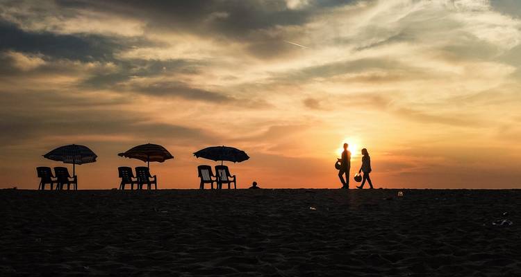 Een strandtafereel bij zonsondergang met silhouetten van mensen en parasols.