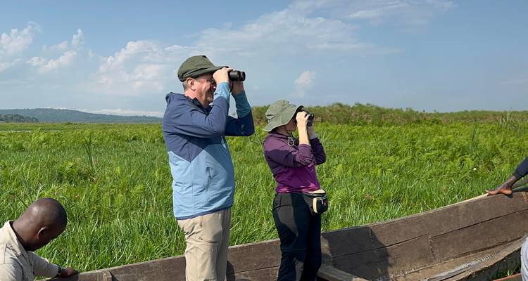 Two tourists using binoculars to view wildlife in a marshland.