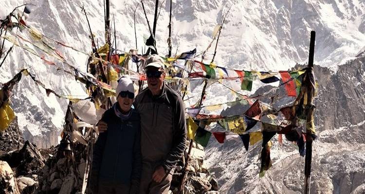 Deux personnes avec des drapeaux de prière et des sommets enneigés.