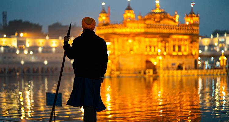 Persona parada frente al Templo Dorado por la noche.