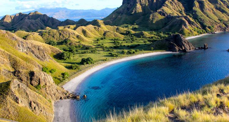 Aerial view of a beach crescent with turquoise waters and lush hills.