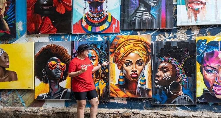 Reisender zeigt auf eine bunte Straßenkunst-Wand mit afro-inspirierten Porträts