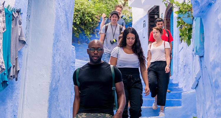 Groupe de touristes marchant dans une rue étroite aux marches peintes en bleu.