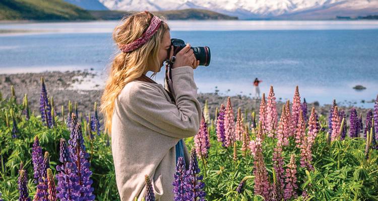 Photographe femme prenant des photos de fleurs au bord d'un lac avec des montagnes.