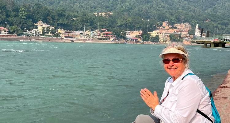 A woman smiling and sitting by a river with buildings in the background.