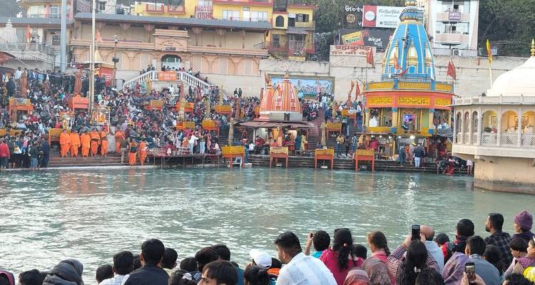 A busy ghat with many people and a temple along the river.